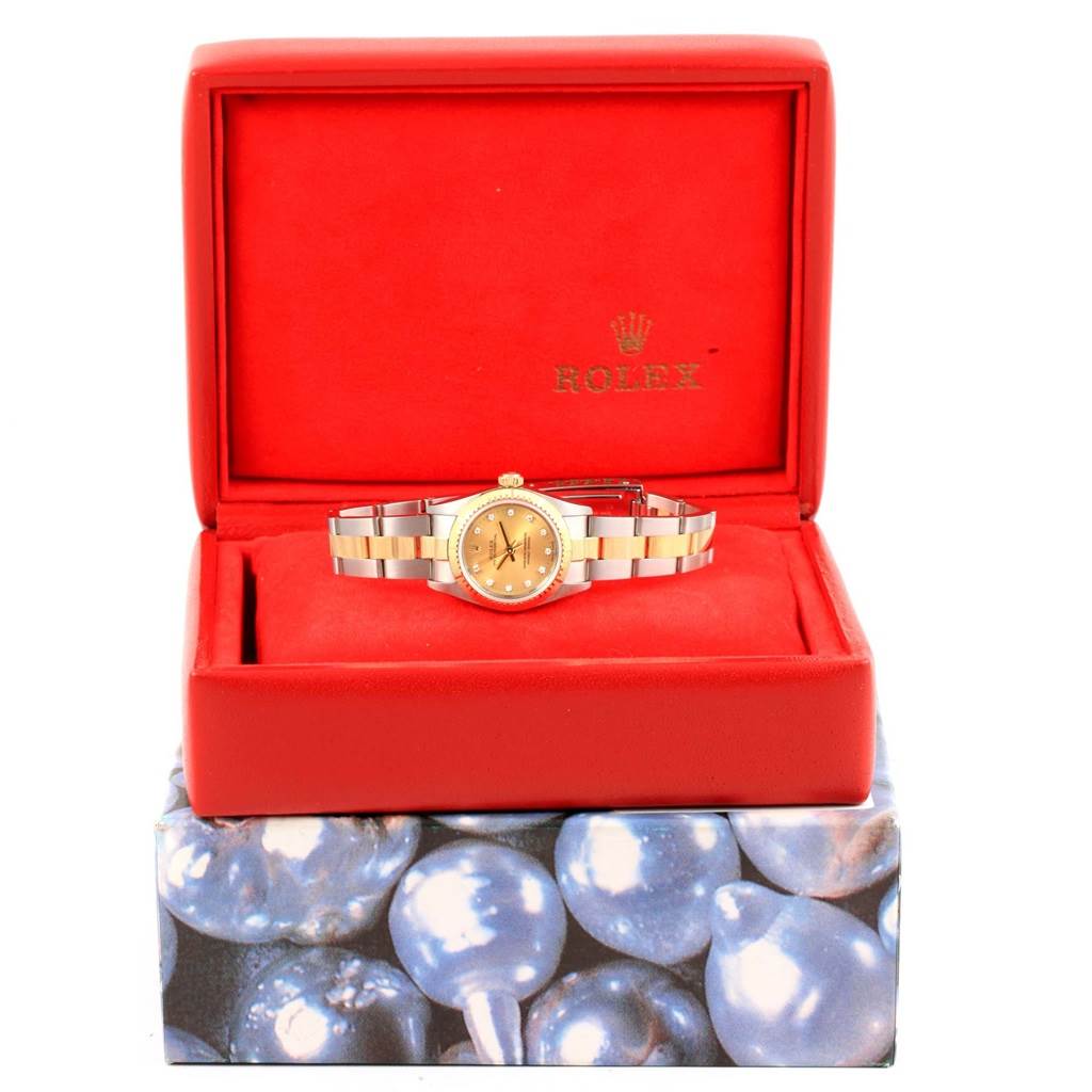 The Rolex Oyster Perpetual 76243 Women's Steel and Gold (two tone) Champagne Dial 76243 Women's Steel and Gold (two tone) Champagne Dial watch is shown front-facing in an open red box with a bracelet visible and a pearl-themed outer packaging.