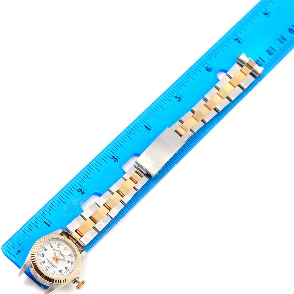 The image shows a Rolex Oyster Perpetual 67193 Women
s Steel and Gold (two tone) White Dial 67193 Women
s Steel and Gold (two tone) White Dial watch laid flat with a blue ruler measuring its length.