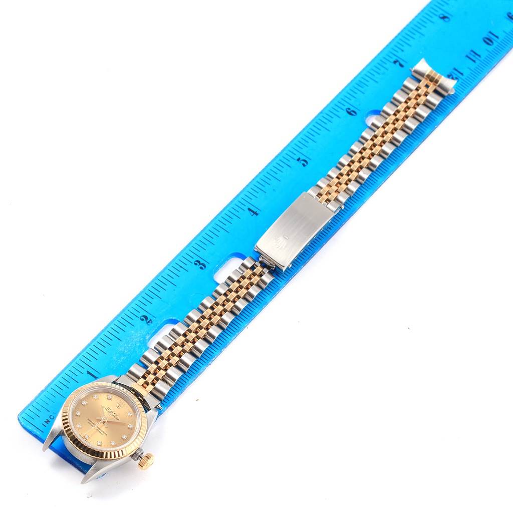 The Rolex Oyster Perpetual 67193 Women's Steel and Gold (two tone) Champagne Dial 67193 Women's Steel and Gold (two tone) Champagne Dial watch is displayed flat with a blue ruler for scale, showcasing the face, bracelet, and clasp.