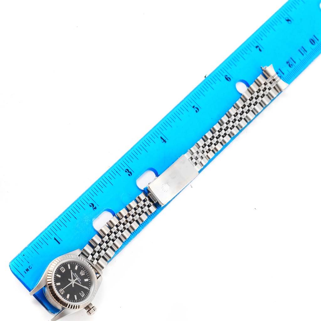 This image shows a Rolex Oyster Perpetual 76094 Women's Stainless Steel Black Dial 76094 Women's Stainless Steel Black Dial watch laid out flat beside a ruler.