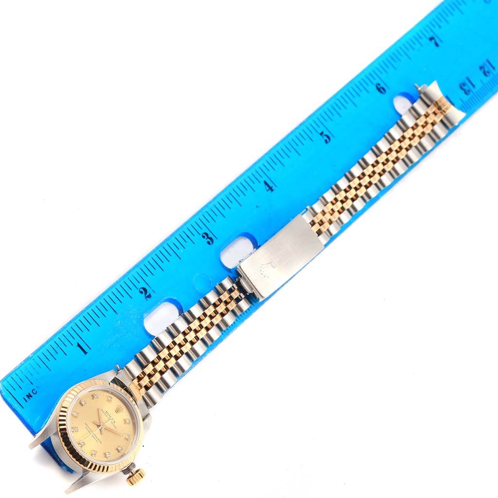 The image shows a top-down view of a Rolex Oyster Perpetual 67193 Women's Steel and Gold (two tone) Champagne Dial 67193 Women's Steel and Gold (two tone) Champagne Dial watch with its bracelet and clasp aligned with a blue ruler.