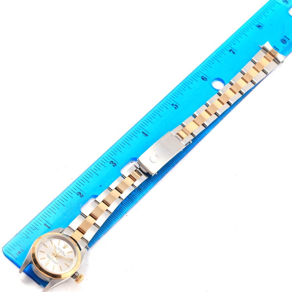 The Rolex Oyster Perpetual 76183 Women's Steel and Gold (two tone) Silver Dial 76183 Women's Steel and Gold (two tone) Silver Dial watch is shown flat from above, displayed alongside a ruler to measure its length.