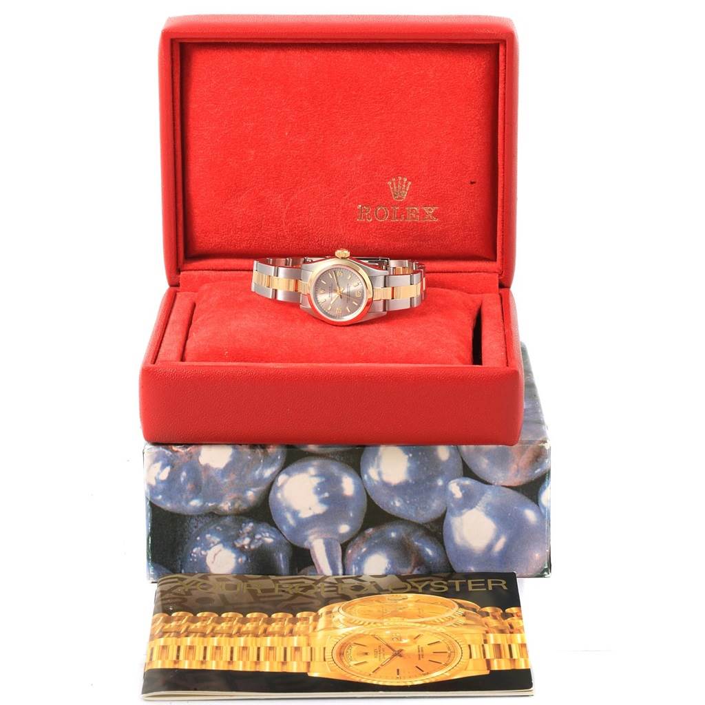 The image shows a Rolex Oyster Perpetual 67183 Women's Steel and Gold (two tone) Grey Dial 67183 Women's Steel and Gold (two tone) Grey Dial watch in its red case, placed on a box, accompanied by an instruction booklet.