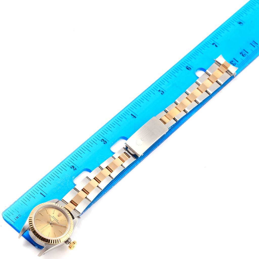 The image shows a Rolex Oyster Perpetual 67193 Women's Steel and Gold (two tone) Champagne Dial 67193 Women's Steel and Gold (two tone) Champagne Dial watch placed next to a blue ruler to measure its length, showing the face, bezel, and bracelet.