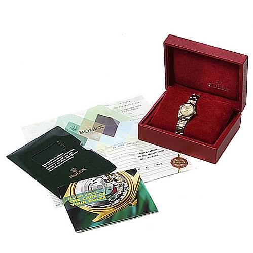The image shows a Rolex Oyster Perpetual 76183 Women's Stainless Steel Champagne Dial 76183 Women's Stainless Steel Champagne Dial watch angled from the top, along with its red case and accompanying certificates and booklets.