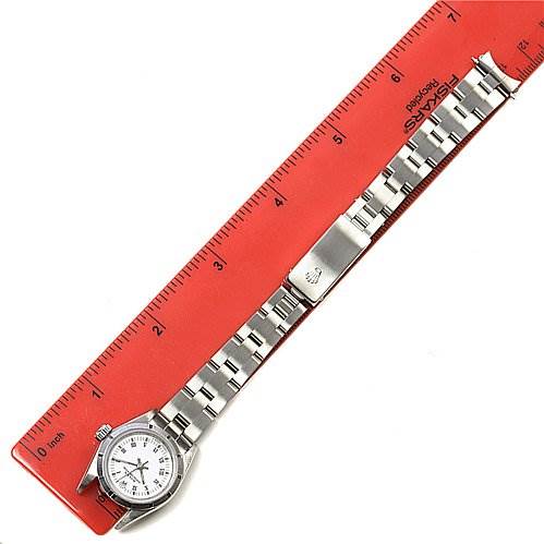 The image shows a Rolex Oyster Perpetual 67230 Women's Stainless Steel White Dial 67230 Women's Stainless Steel White Dial watch laid flat next to a red ruler at a top-down angle.