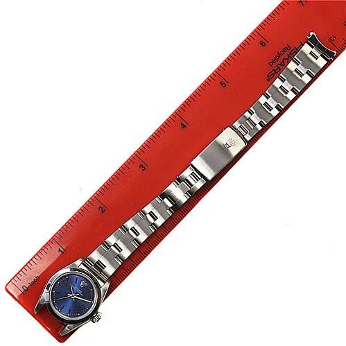 This image shows a Rolex Oyster Perpetual 67180 Women's Stainless Steel Blue Dial 67180 Women's Stainless Steel Blue Dial watch laid flat next to a red ruler, displaying its face, bracelet, and clasp.