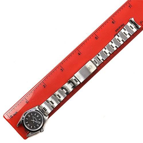 The Rolex Oyster Perpetual 67180 Women's Stainless Steel Black Dial 67180 Women's Stainless Steel Black Dial watch is shown from a top-down angle, displaying its face, bracelet, and clasp next to a red ruler.