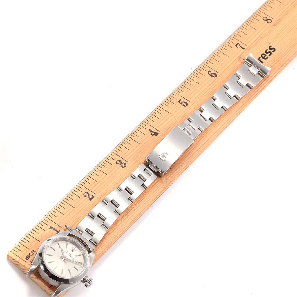 The image shows a flat-laid Rolex Oyster Perpetual 76080 Women
s Stainless Steel Silver Dial 76080 Women
s Stainless Steel Silver Dial watch with its bracelet extended alongside a ruler.