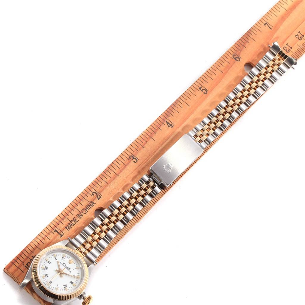 The image shows a Rolex Oyster Perpetual 67193 Women
s Steel and Gold (two tone) White Dial 67193 Women
s Steel and Gold (two tone) White Dial watch laid flat next to a ruler, showcasing its face, bracelet, and clasp.