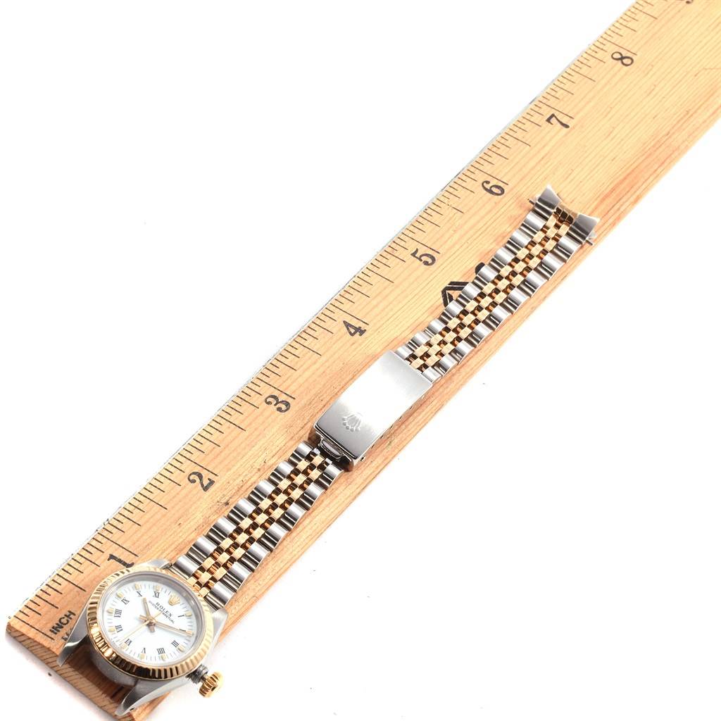 The image shows an overhead view of a Rolex Oyster Perpetual 67193 Women
s Steel and Gold (two tone) White Dial 67193 Women
s Steel and Gold (two tone) White Dial watch with a two-tone bracelet next to a wooden ruler.