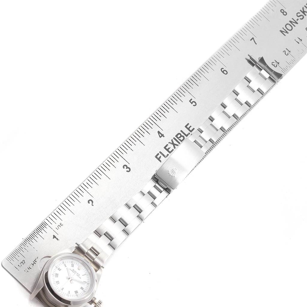 The image shows a Rolex Oyster Perpetual 67180 Women's Stainless Steel White Dial 67180 Women's Stainless Steel White Dial watch partially under a metal ruler, displaying its bracelet and clasp.