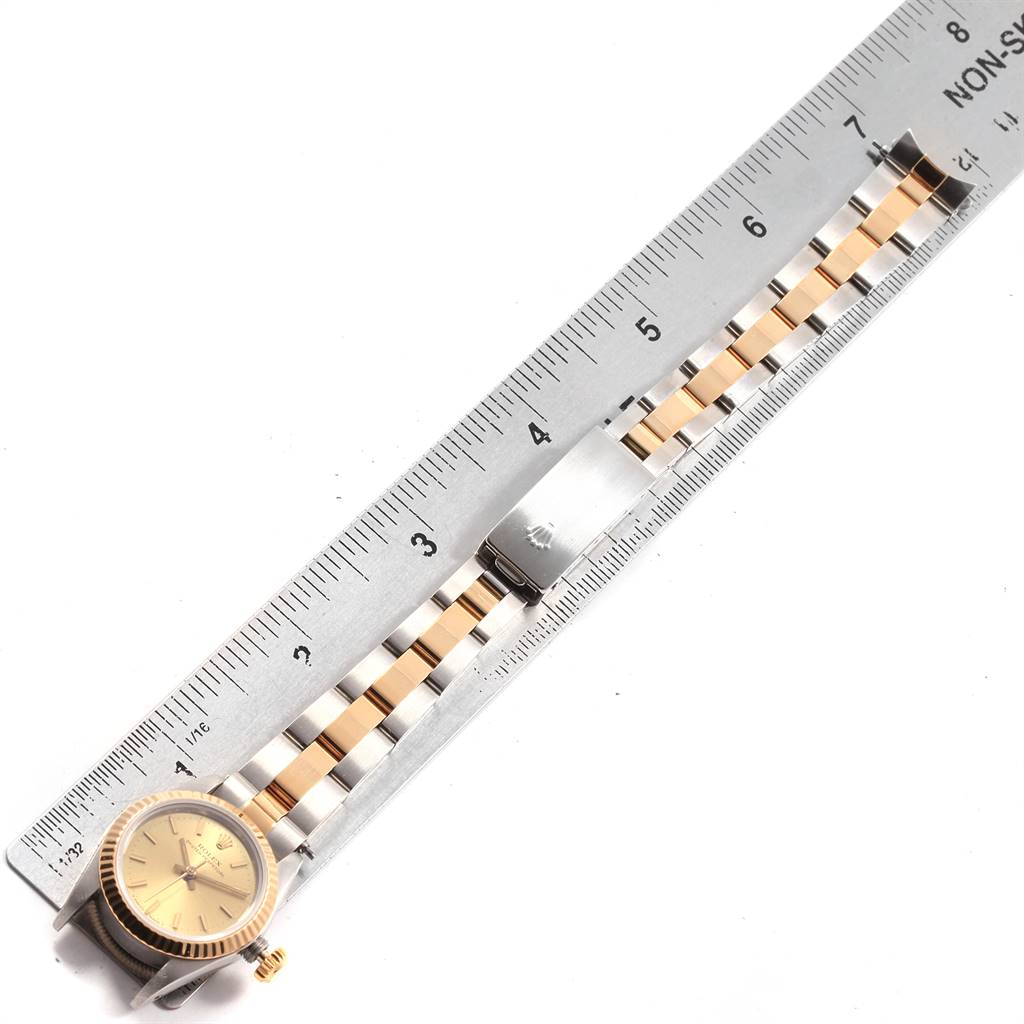 The Rolex Oyster Perpetual 67193 Women
s Steel and Gold (two tone) Champagne Dial 67193 Women
s Steel and Gold (two tone) Champagne Dial watch is shown laying flat with its face and two-tone bracelet next to a ruler.