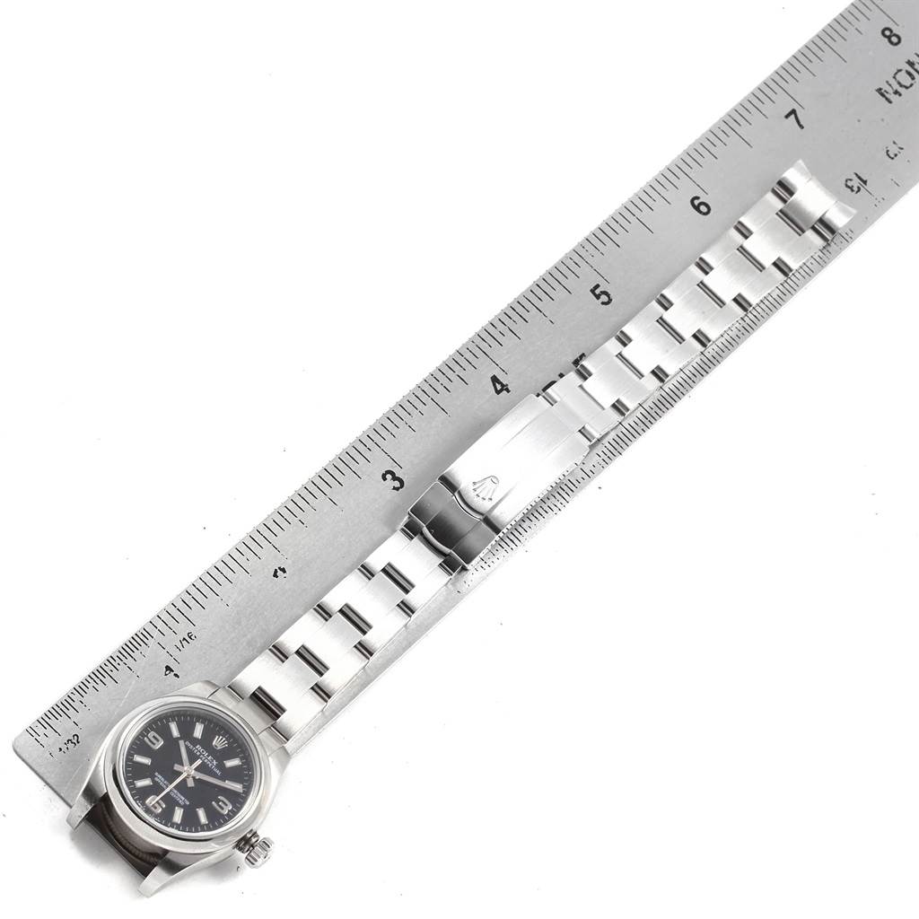 The image shows a top view of a Rolex Oyster Perpetual 176200 Women
s Stainless Steel Black Dial 176200 Women
s Stainless Steel Black Dial watch, highlighting its face, clasp, and bracelet next to a ruler for scale.