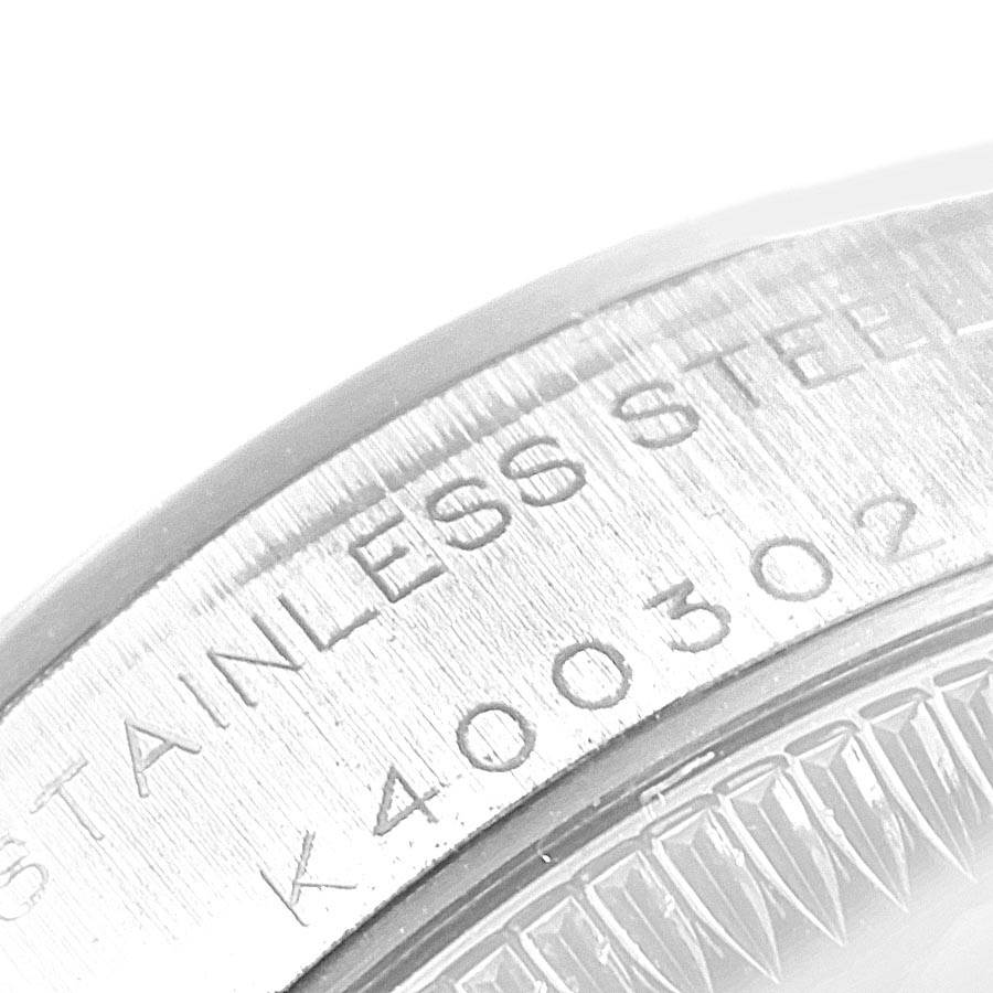 The image shows a close-up of the edge of a Rolex Oyster Perpetual 76080 Women's Stainless Steel Black Dial 76080 Women's Stainless Steel Black Dial watch, highlighting the "STAINLESS STEEL" engraving and serial number.