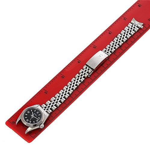 The image shows a Rolex Oyster Perpetual 76094 Women's Stainless Steel Black Dial 76094 Women's Stainless Steel Black Dial watch laid flat, displaying the face, bezel, and full bracelet on top of a red ruler.