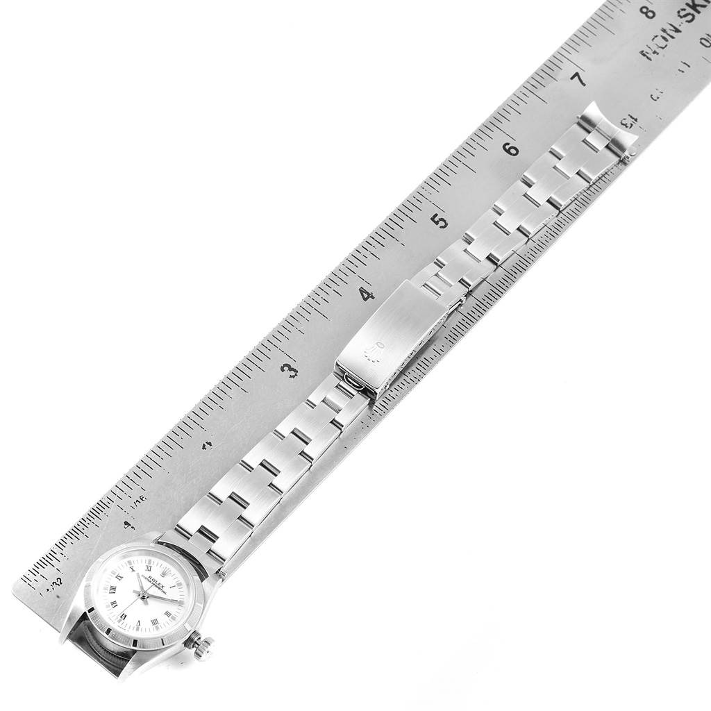 The Rolex Oyster Perpetual 67230 Women's Stainless Steel White Dial 67230 Women's Stainless Steel White Dial watch is shown from a top-down angle, displaying the watch face, metal bracelet, and clasp alongside a ruler for scale.