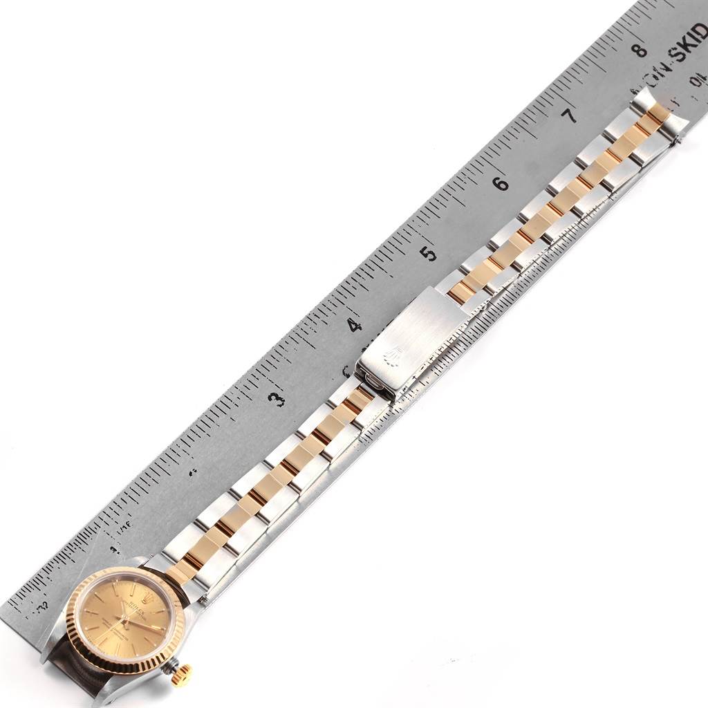 The Rolex Oyster Perpetual 67193 Women
s Steel and Gold (two tone) Champagne Dial 67193 Women
s Steel and Gold (two tone) Champagne Dial watch is shown from the top, displaying its face, crown, and bracelet fully extended next to a ruler.