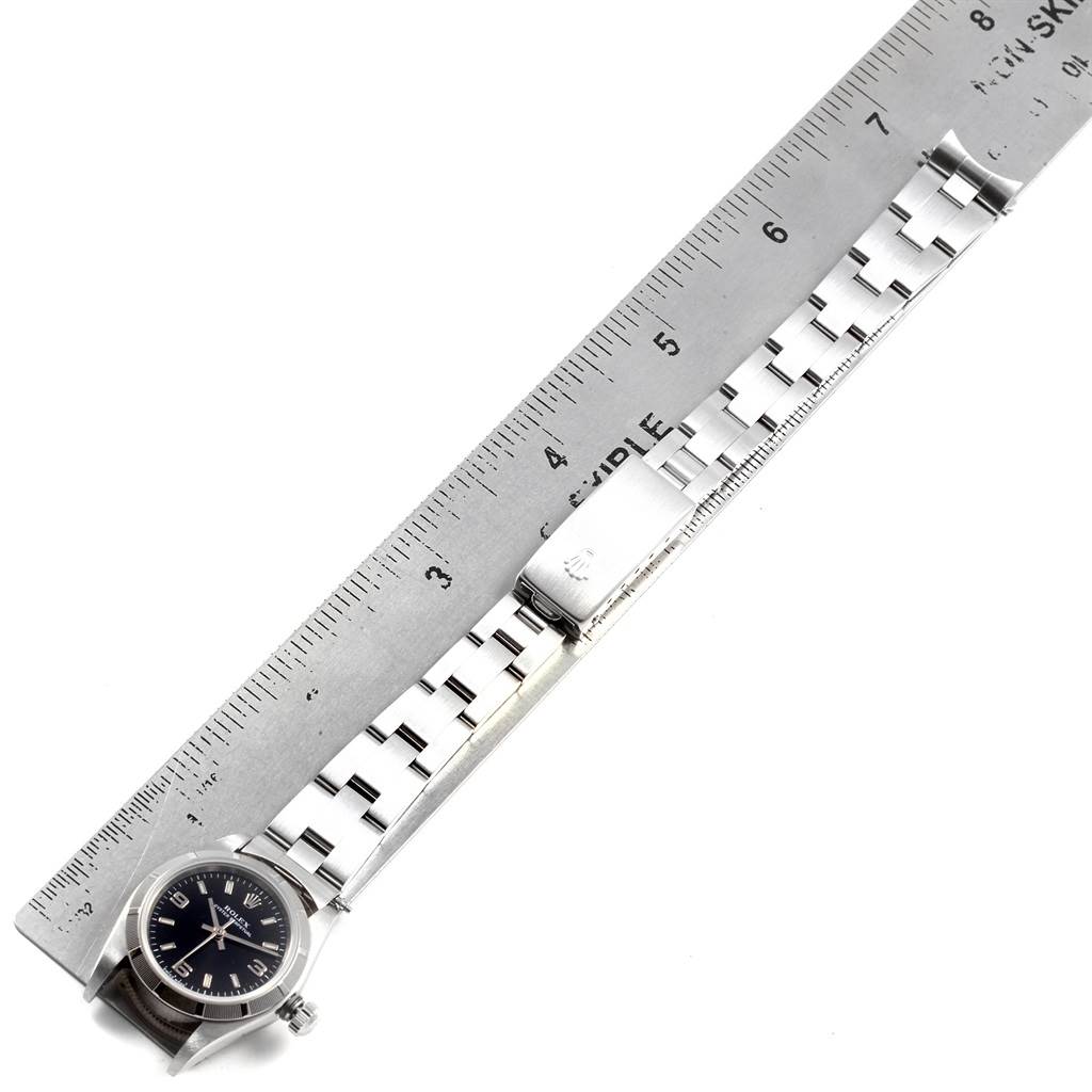 This image shows a Rolex Oyster Perpetual 76030 Women
s Stainless Steel Black Dial 76030 Women
s Stainless Steel Black Dial watch laid flat next to a ruler, highlighting the watch face, bezel, and metal bracelet.