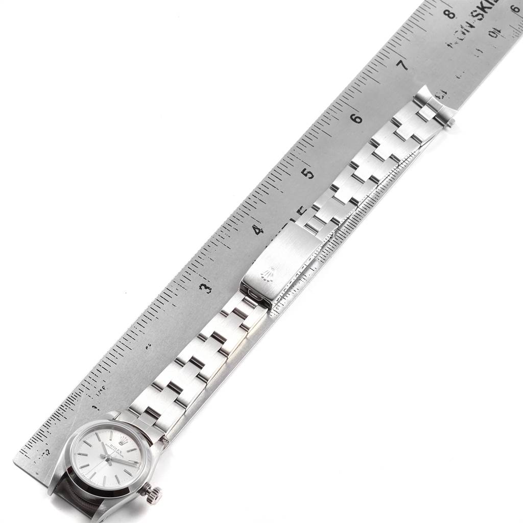 This image shows a top view of a Rolex Oyster Perpetual 67180 Women
s Stainless Steel Silver Dial 67180 Women
s Stainless Steel Silver Dial watch alongside a ruler, highlighting the watch
s bracelet and clasp.