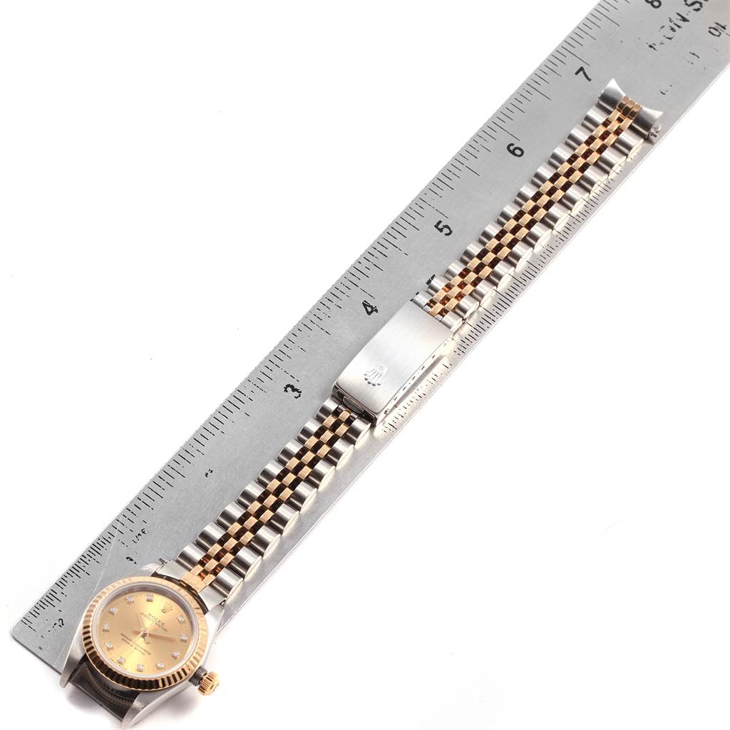 The Rolex Oyster Perpetual 76193 Women
s Steel and Gold (two tone) Champagne Dial 76193 Women
s Steel and Gold (two tone) Champagne Dial watch is shown from a top view, highlighting its face, bracelet, and clasp next to a ruler.