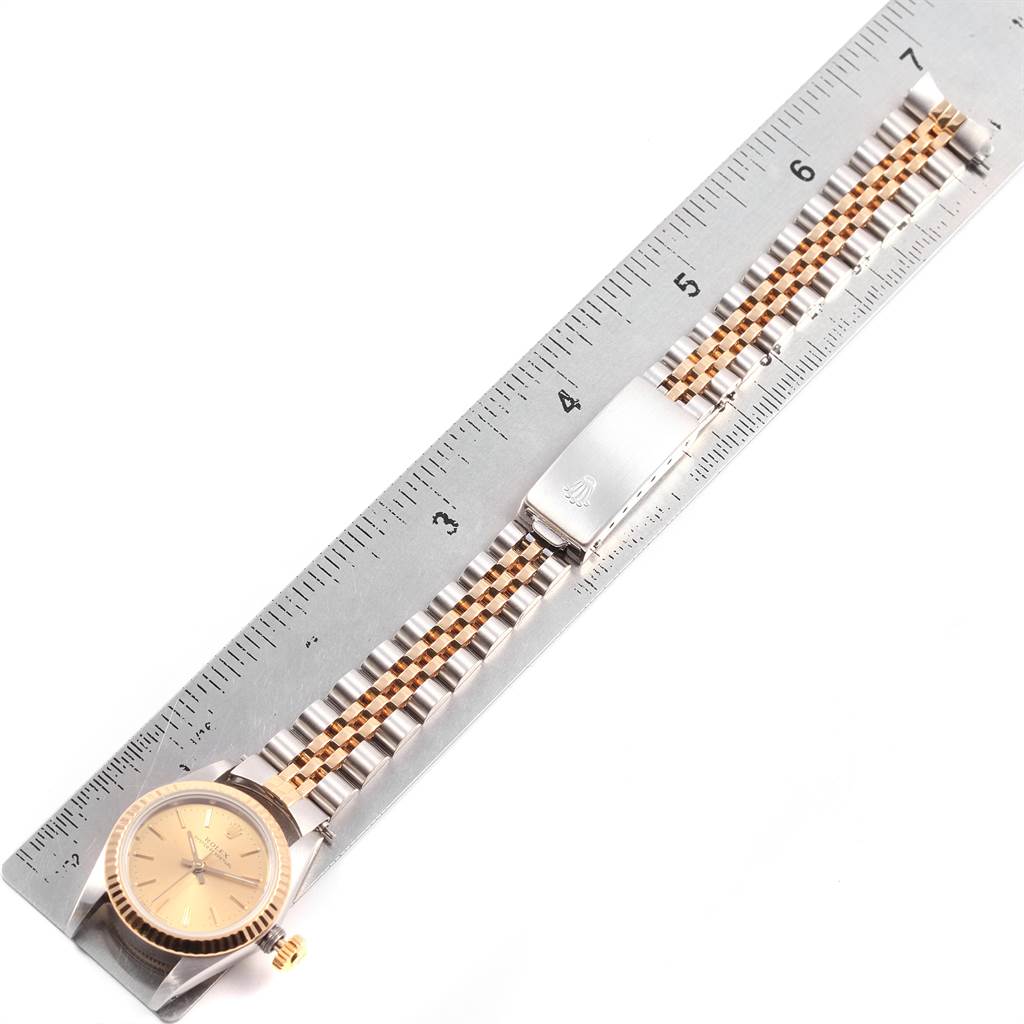 The image shows an overhead view of a Rolex Oyster Perpetual 67193 Women's Steel and Gold (two tone) Champagne Dial 67193 Women's Steel and Gold (two tone) Champagne Dial watch, with its casing, bezel, dial, and full bracelet, next to a ruler.