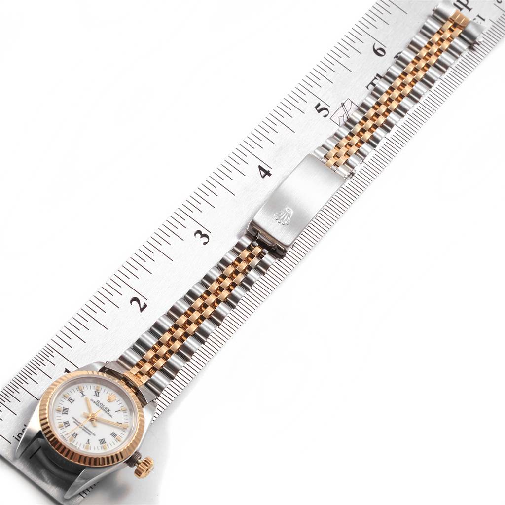 The image shows a top-down view of a Rolex Oyster Perpetual 67193 Women's Steel and Gold (two tone) White Dial 67193 Women's Steel and Gold (two tone) White Dial watch with its bracelet partially extended alongside a ruler.