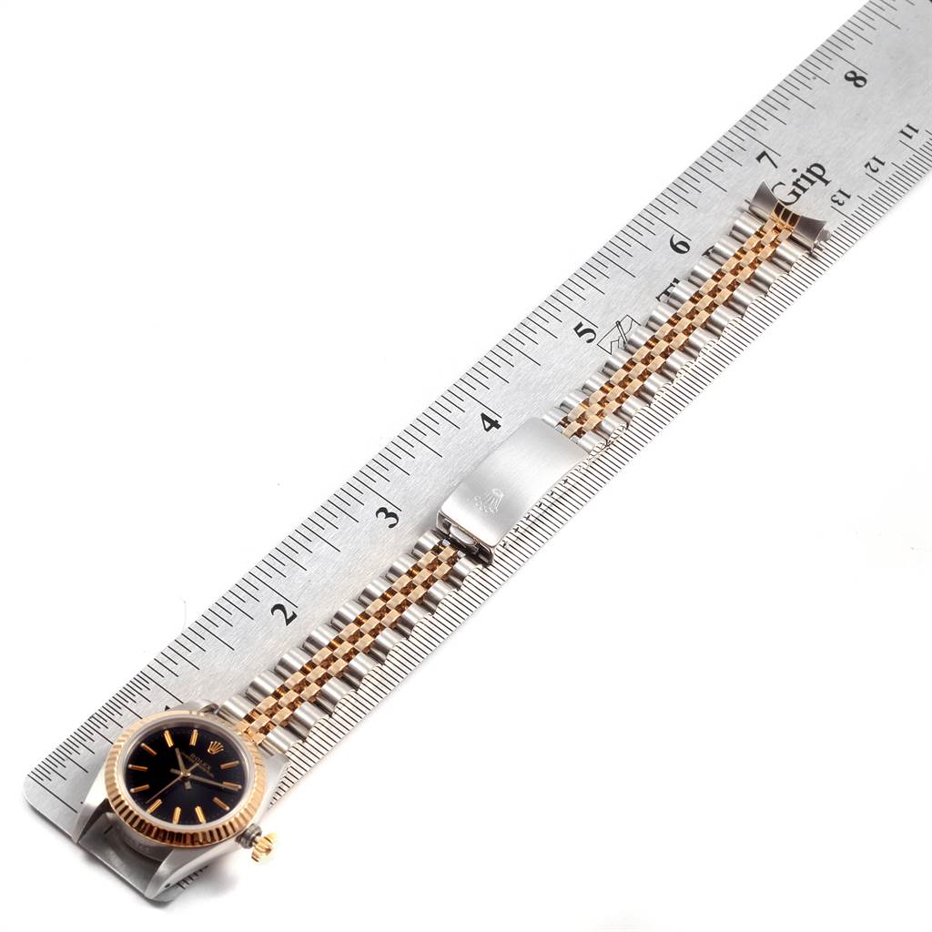 The image shows a Rolex Oyster Perpetual 67193 Women
s Steel and Gold (two tone) Black Dial 67193 Women
s Steel and Gold (two tone) Black Dial watch placed alongside a ruler, highlighting the watch face, bezel, and bracelet.