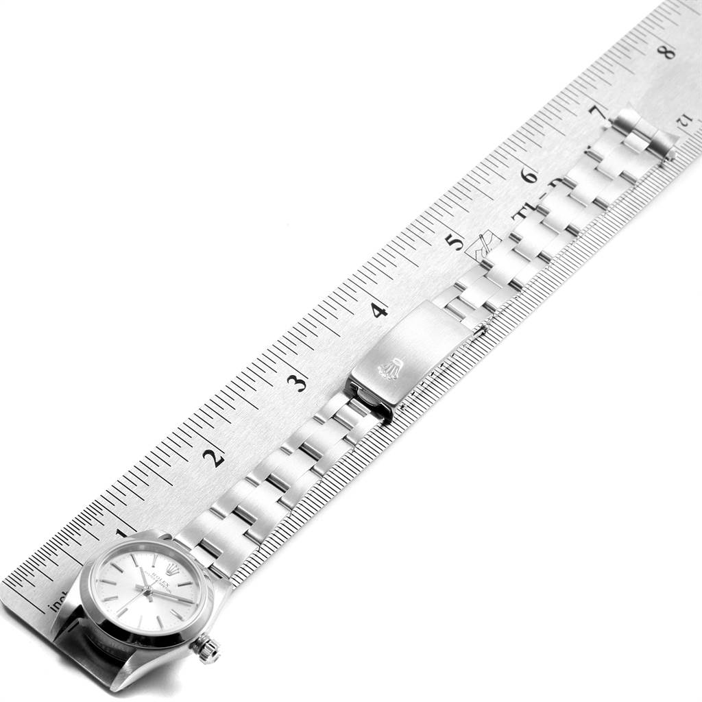 The image shows a side angle of a Rolex Oyster Perpetual 76080 Women's Stainless Steel Silver Dial 76080 Women's Stainless Steel Silver Dial watch alongside a metal ruler, highlighting the face and bracelet.