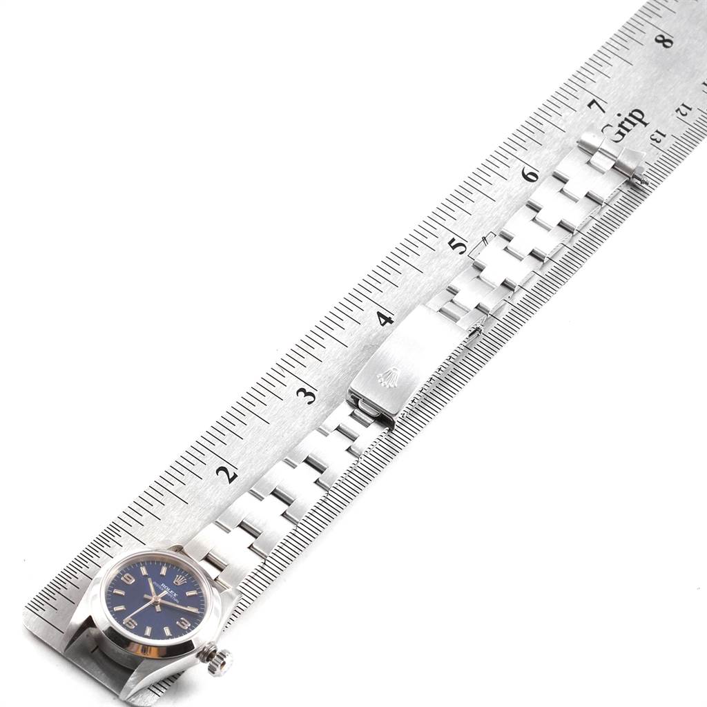 The Rolex Oyster Perpetual 67180 Women
s Stainless Steel Blue Dial 67180 Women
s Stainless Steel Blue Dial watch is shown from a top angle, displaying the face, bracelet band, and clasp alongside a ruler.