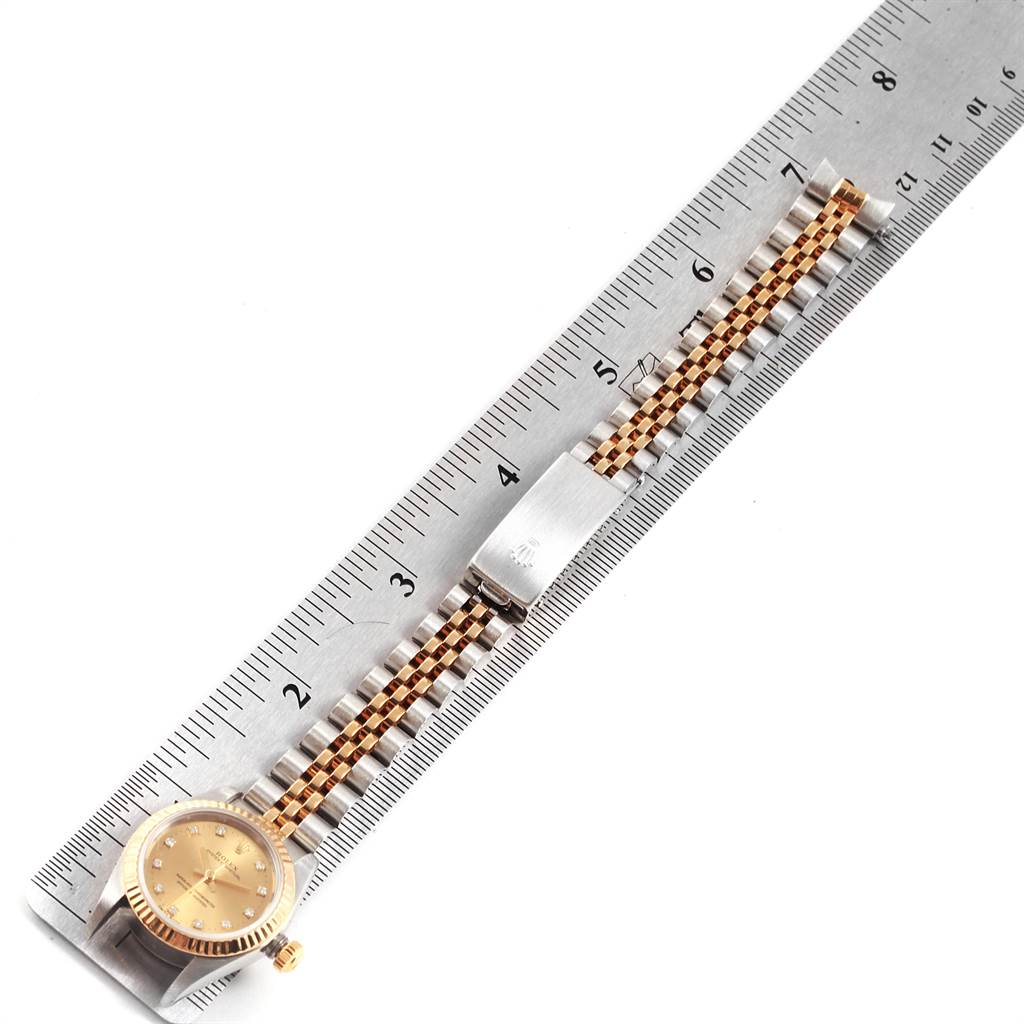 The image shows a top view of a Rolex Oyster Perpetual 76193 Women
s Steel and Gold (two tone) Champagne Dial 76193 Women
s Steel and Gold (two tone) Champagne Dial watch, highlighting its face, bezel, and partially extended bracelet.