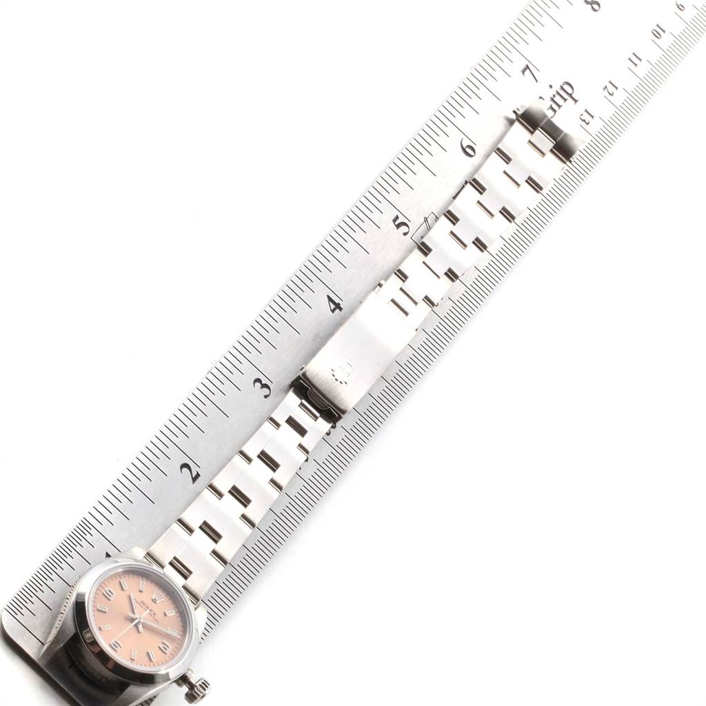 The image shows the Rolex Oyster Perpetual 67180 Women's Stainless Steel Pink Dial 67180 Women's Stainless Steel Pink Dial watch laid next to a ruler, displaying the face and bracelet.