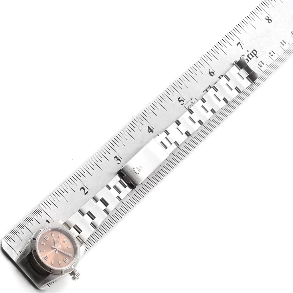 The image shows an angled view of a Rolex Oyster Perpetual 76030 Women's Stainless Steel Pink Dial 76030 Women's Stainless Steel Pink Dial watch, highlighting its clasp, bracelet, and dial against a ruler backdrop.