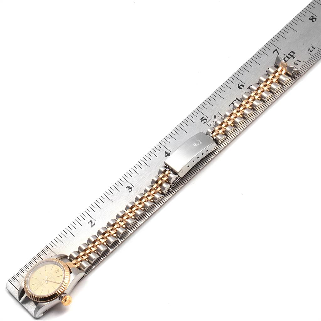 This image shows a Rolex Oyster Perpetual 76193 Women's Steel and Gold (two tone) Champagne Dial 76193 Women's Steel and Gold (two tone) Champagne Dial watch placed on a ruler, highlighting the watch face, bracelet, and clasp.