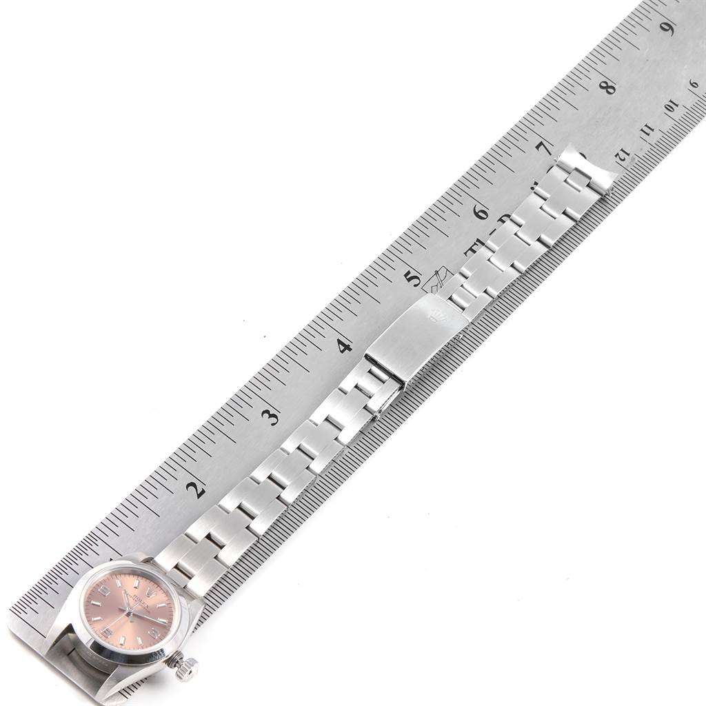 The image shows a Rolex Oyster Perpetual 67180 Women's Stainless Steel Pink Dial 67180 Women's Stainless Steel Pink Dial watch laid next to a ruler, displaying the face, bracelet, and clasp from a top-down angle.