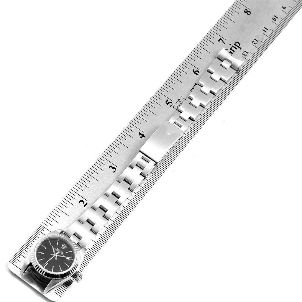 The image shows a Rolex Oyster Perpetual 76094 Women's Stainless Steel Black Dial 76094 Women's Stainless Steel Black Dial watch laid out flat next to a ruler, displaying the watch face and bracelet.