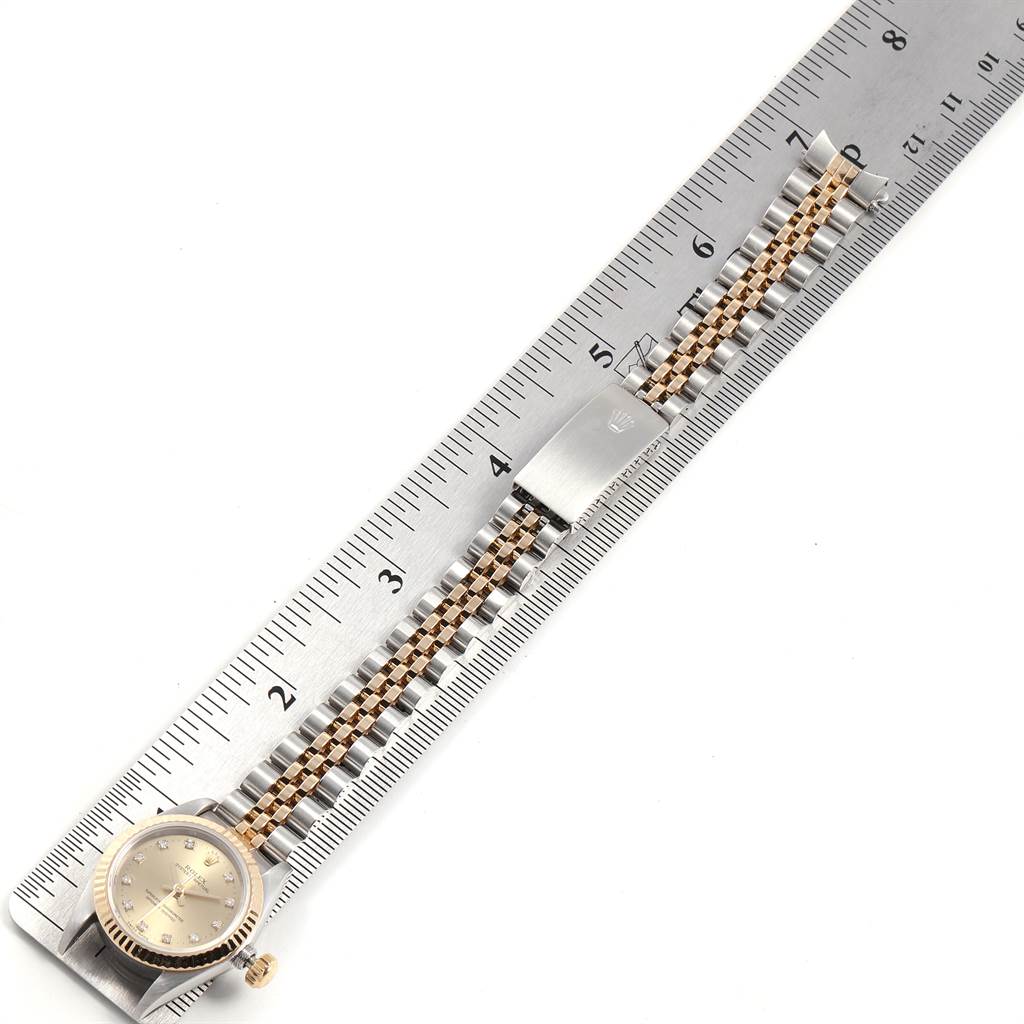 This image shows a Rolex Oyster Perpetual 67193 Women's Steel and Gold (two tone) Champagne Dial 67193 Women's Steel and Gold (two tone) Champagne Dial watch laying flat with its two-tone bracelet extended along a ruler.