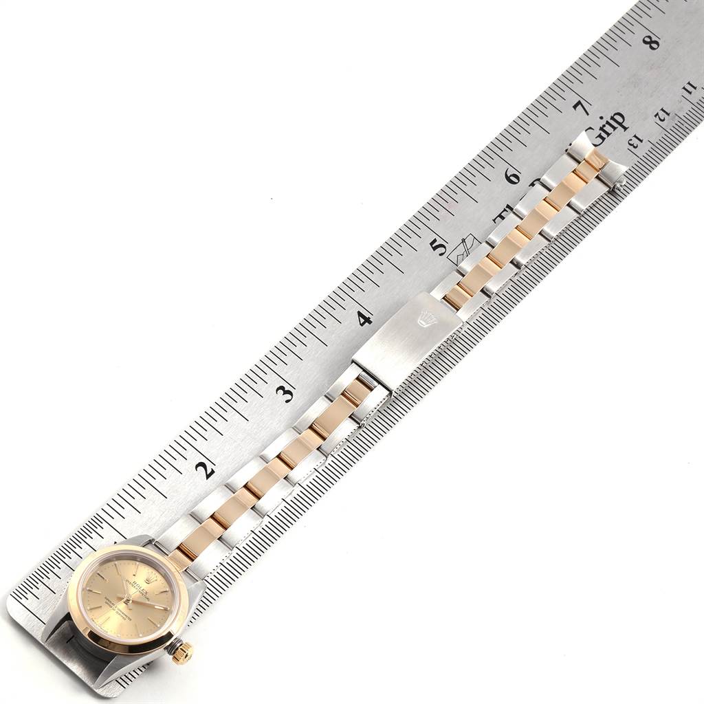 The image shows a Rolex Oyster Perpetual 76183 Women
s Steel and Gold (two tone) Champagne Dial 76183 Women
s Steel and Gold (two tone) Champagne Dial watch laid flat next to a ruler, displaying the face and bracelet.