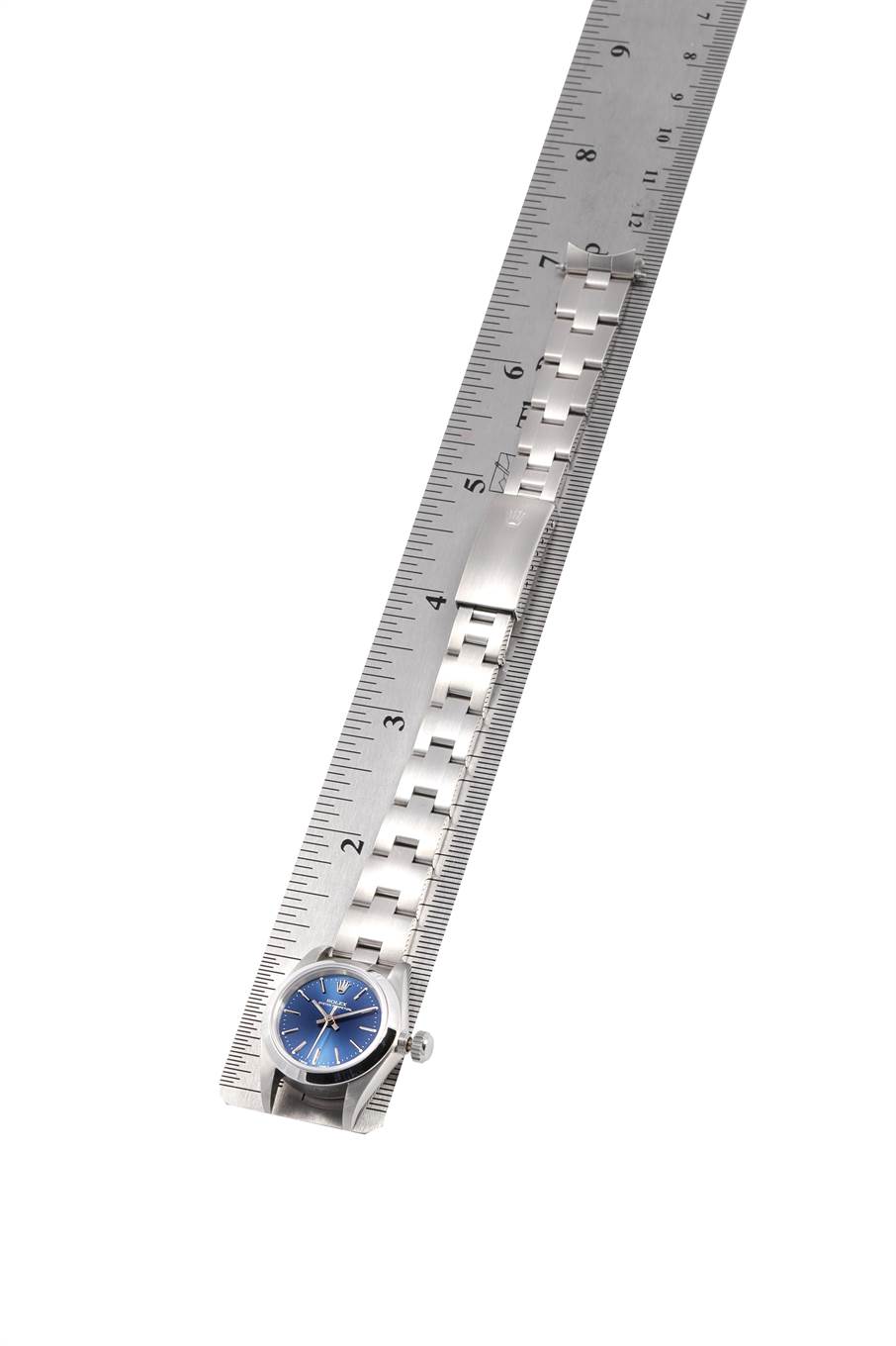 This image shows a Rolex Oyster Perpetual 67180 Women's Stainless Steel Blue Dial 67180 Women's Stainless Steel Blue Dial watch lying flat next to a ruler, highlighting its strap and face.
