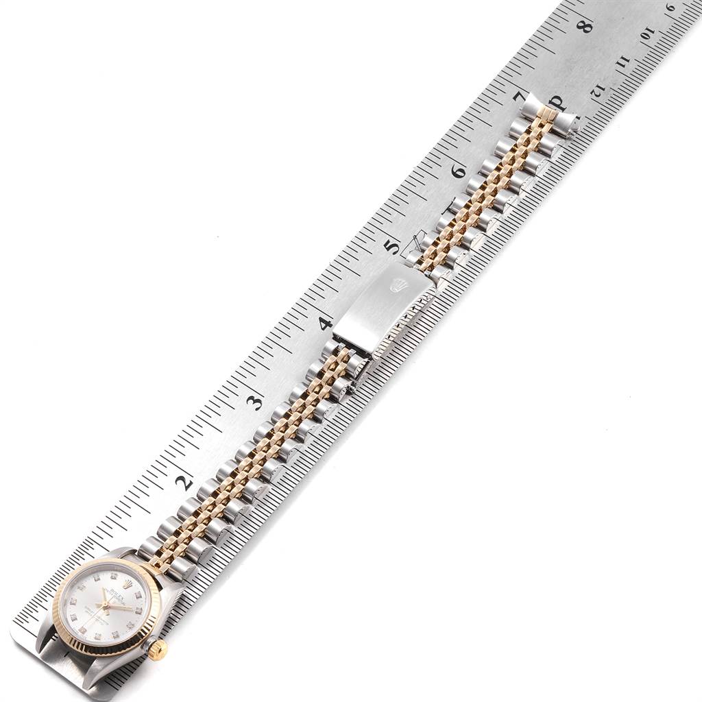 The Rolex Oyster Perpetual 76193 Women's Steel and Gold (two tone) Silver Dial 76193 Women's Steel and Gold (two tone) Silver Dial watch is shown lying flat with the face, bracelet, and clasp visible, measured against a metal ruler.