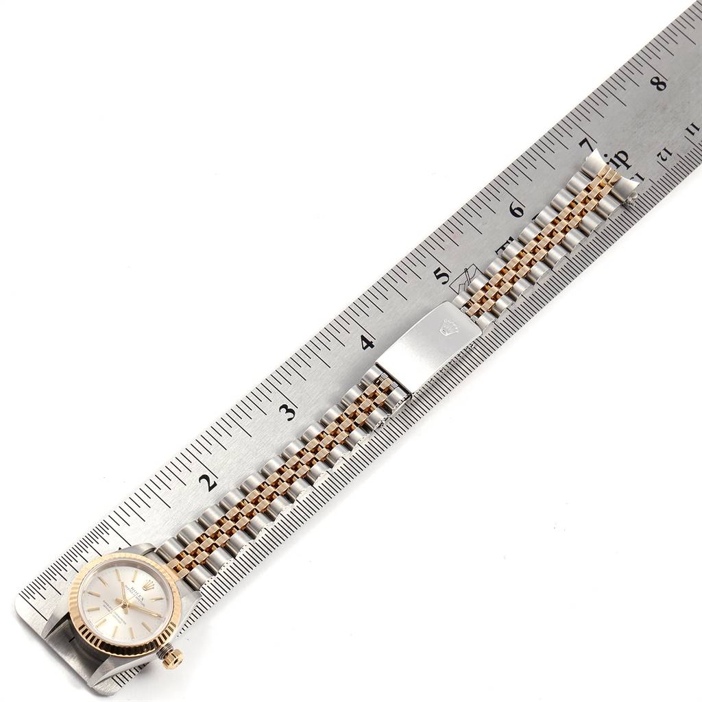 The image shows a Rolex Oyster Perpetual 76193 Women's Steel and Gold (two tone) Silver Dial 76193 Women's Steel and Gold (two tone) Silver Dial watch placed next to a ruler, displaying its bracelet and face from a top view angle.