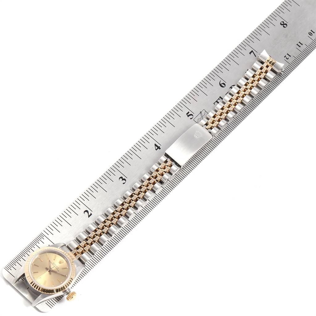 A Rolex Oyster Perpetual 67193 Women
s Steel and Gold (two tone) Champagne Dial 67193 Women
s Steel and Gold (two tone) Champagne Dial watch is shown in a flat-lay view, displaying the dial, bezel, bracelet, and clasp on a ruler.
