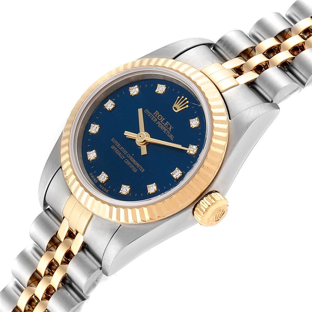 The image shows a Rolex Oyster Perpetual 76193 Women
s Steel and Gold (two tone) Blue Dial 76193 Women
s Steel and Gold (two tone) Blue Dial watch at an angle displaying its blue dial, gold bezel, crown, and part of its metal band.