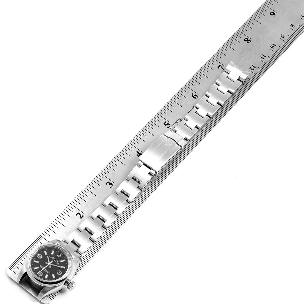 The image shows a top-down view of a Rolex Oyster Perpetual 176200 Women
s Stainless Steel Black Dial 176200 Women
s Stainless Steel Black Dial watch with its metal bracelet stretched out alongside a ruler.