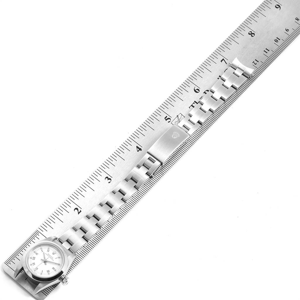 This image shows a Rolex Oyster Perpetual 76080 Women
s Stainless Steel White Dial 76080 Women
s Stainless Steel White Dial watch and its clasp laid out along a ruler, viewed from above.