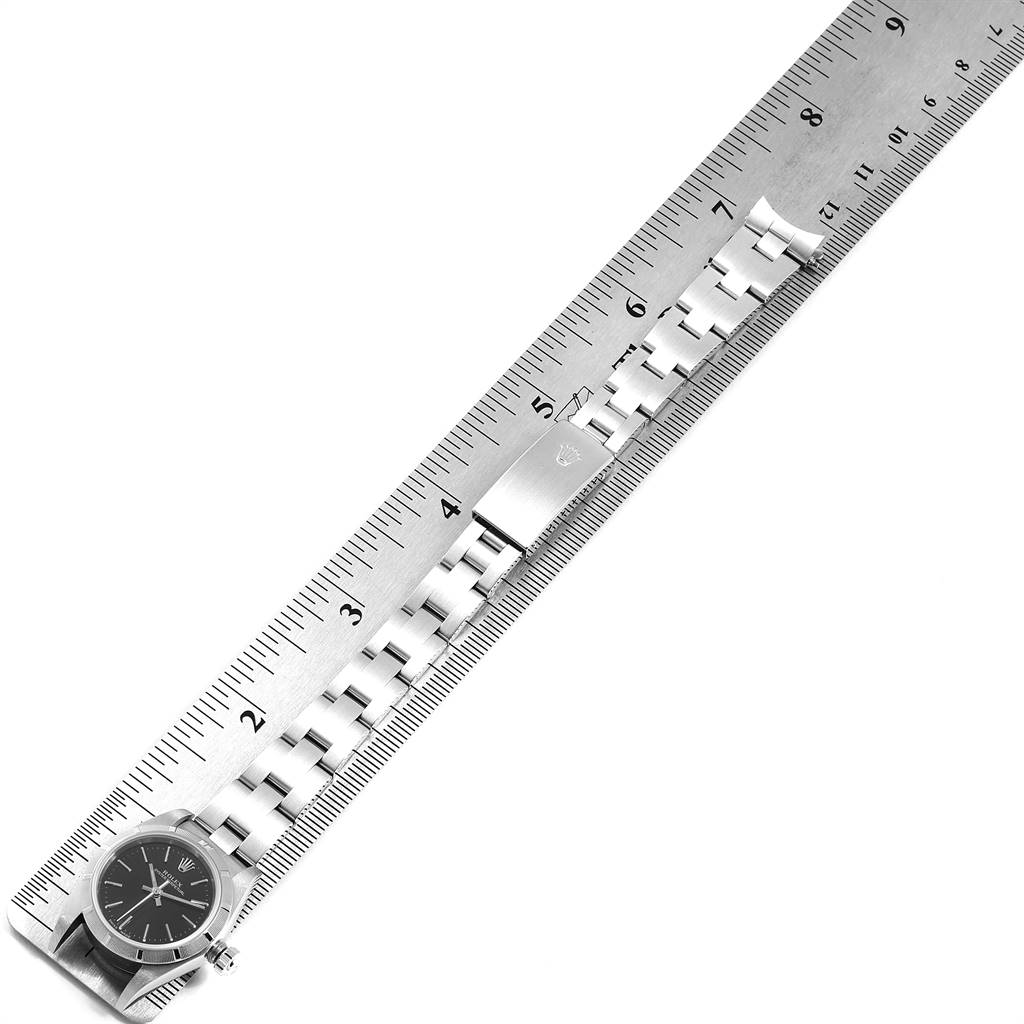 The image shows a Rolex Oyster Perpetual 76030 Women's Stainless Steel Black Dial 76030 Women's Stainless Steel Black Dial watch lying flat next to a ruler, displaying its face and metal bracelet clasp.