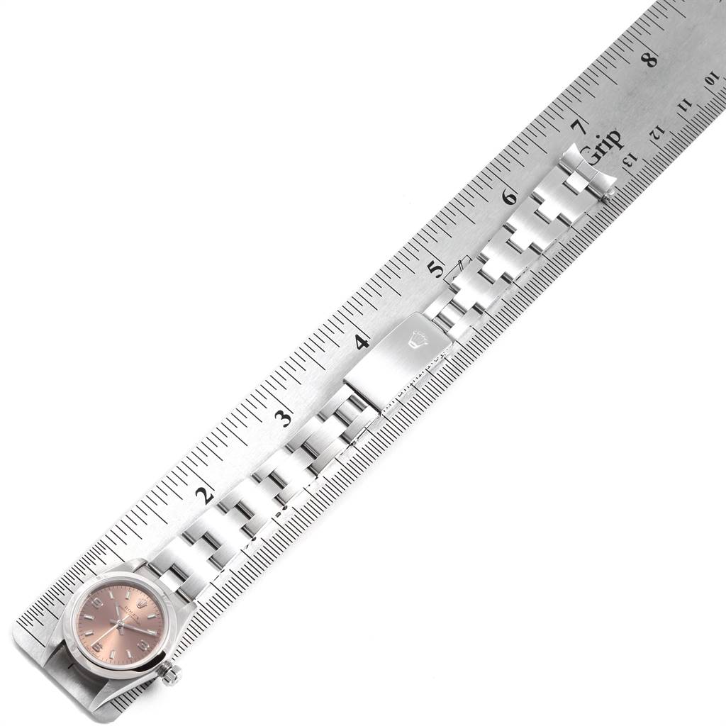 The image shows a Rolex Oyster Perpetual 76080 Women's Stainless Steel Pink Dial 76080 Women's Stainless Steel Pink Dial watch placed next to a ruler, displaying its pink dial and metal bracelet.