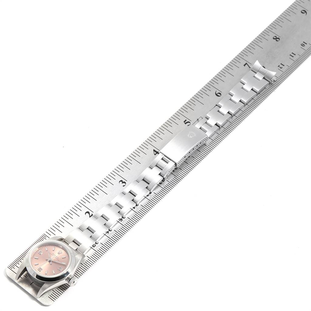 The image shows a Rolex Oyster Perpetual 67180 Women's Stainless Steel Pink Dial 67180 Women's Stainless Steel Pink Dial watch lying flat alongside a metal ruler, displaying its face and band.