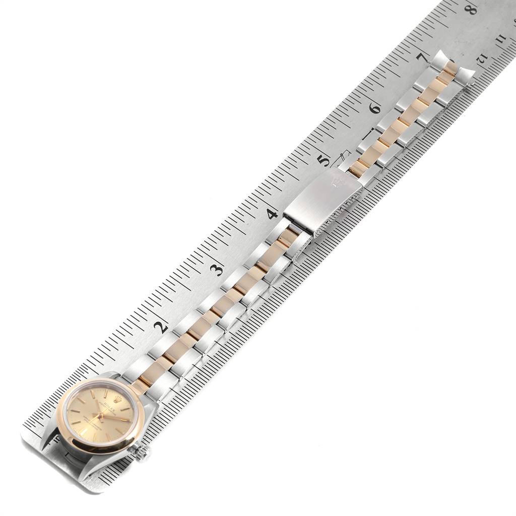 The image shows a Rolex Oyster Perpetual 67183 Women
s Steel and Gold (two tone) Champagne Dial 67183 Women
s Steel and Gold (two tone) Champagne Dial watch placed on a ruler, displaying its face, bracelet, and clasp.