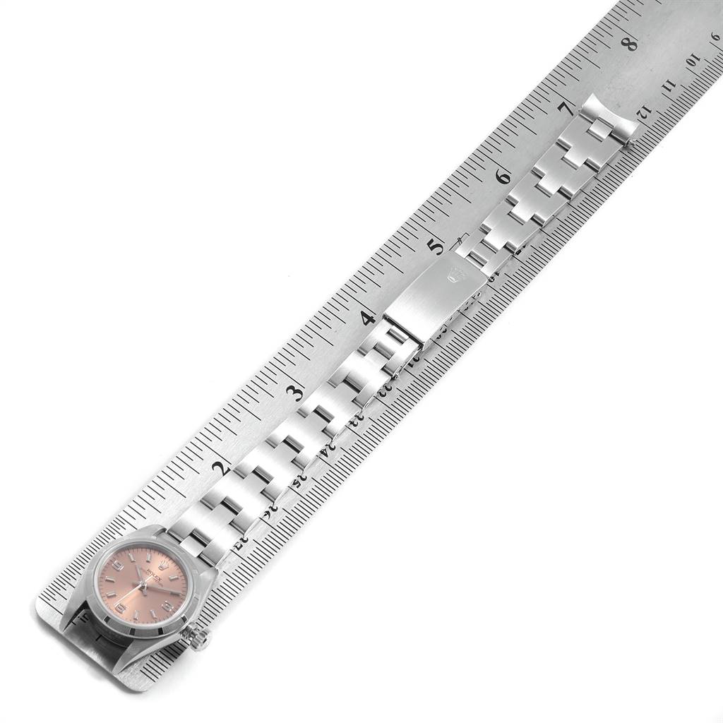 This image shows a Rolex Oyster Perpetual 67230 Women's Stainless Steel Pink Dial 67230 Women's Stainless Steel Pink Dial watch laid flat along a ruler, highlighting the face, bracelet, and clasp.